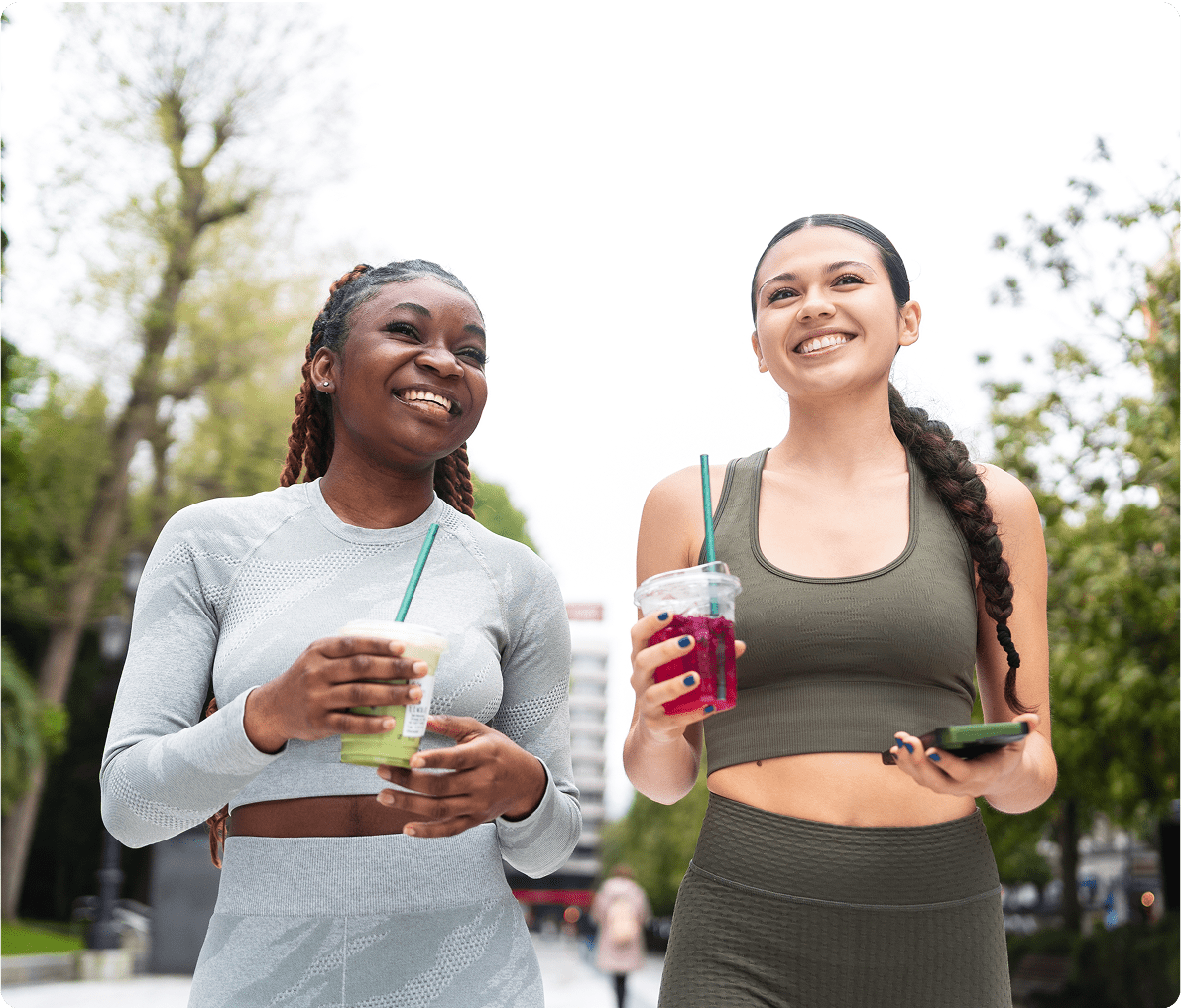 Two women walking, holding drinks, smiling.